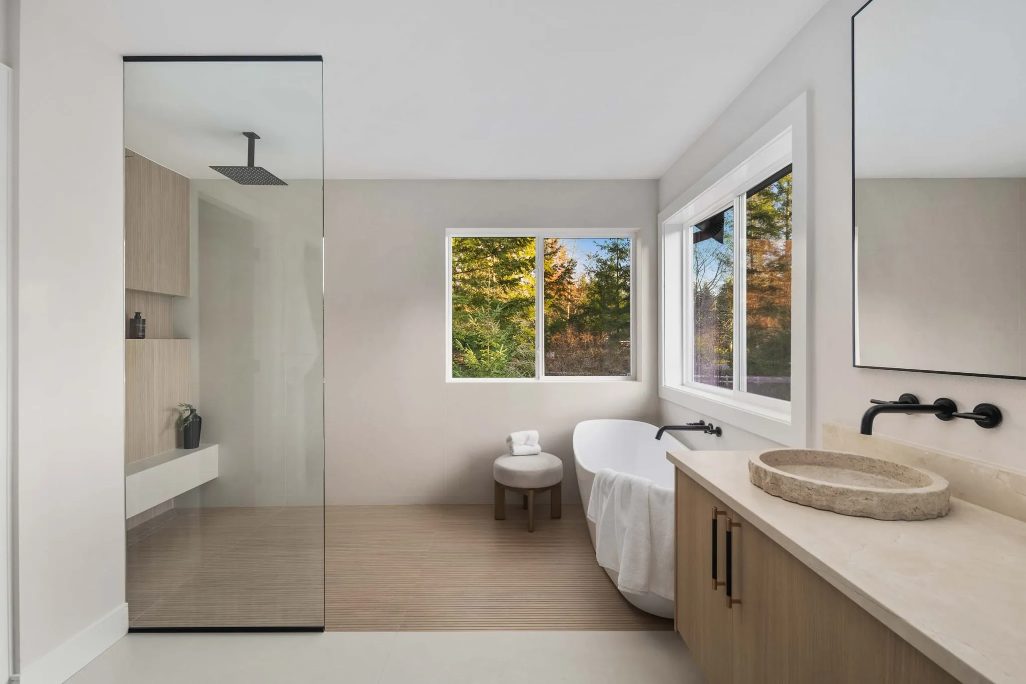 Primary bathroom with a glass walk-in shower, freestanding tub and stone vessel sink, photographed by ACRE Seattle