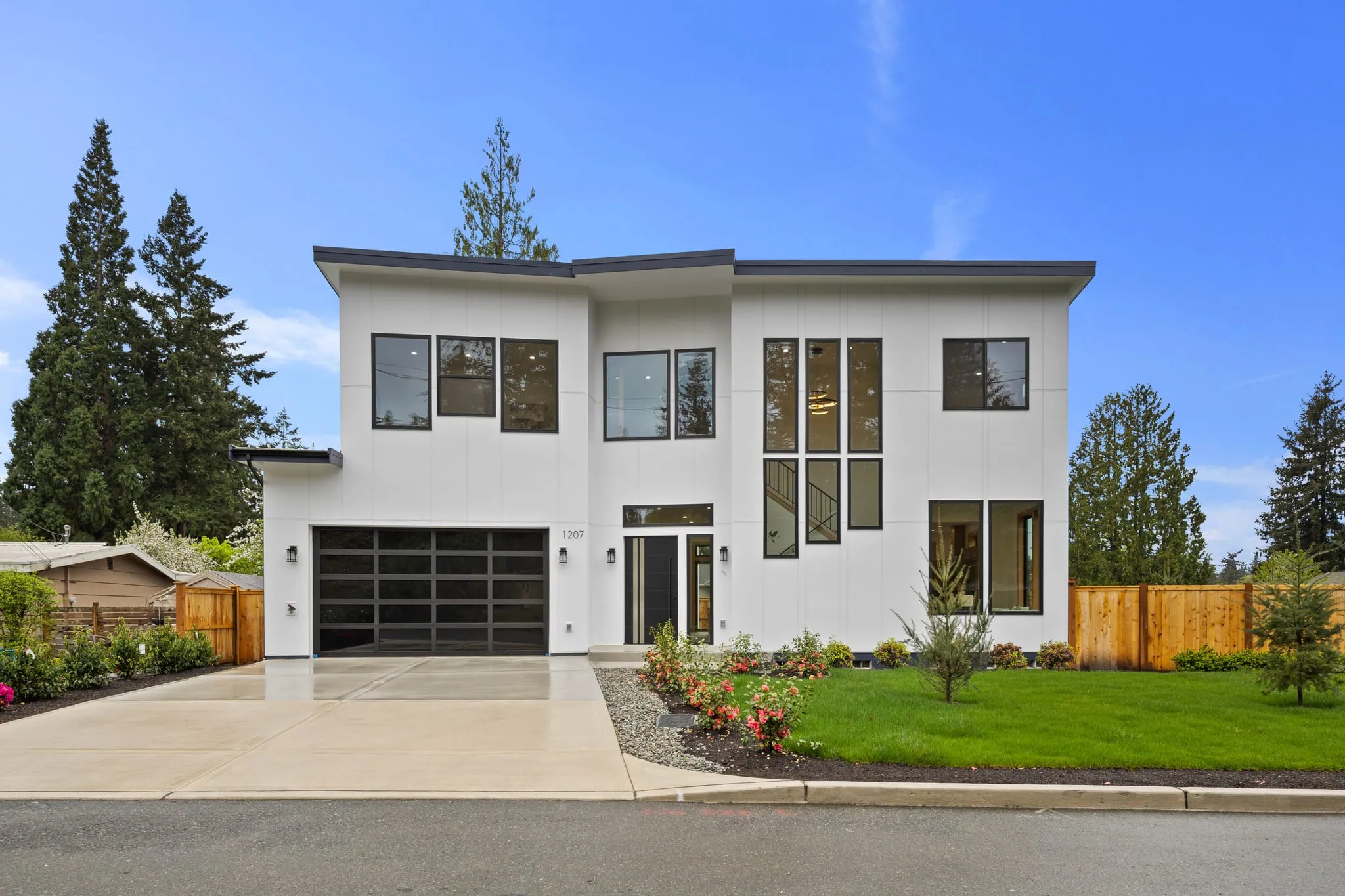 Two-storey white modern home with black-framed windows and a glass garage door, photographed by ACRE Seattle